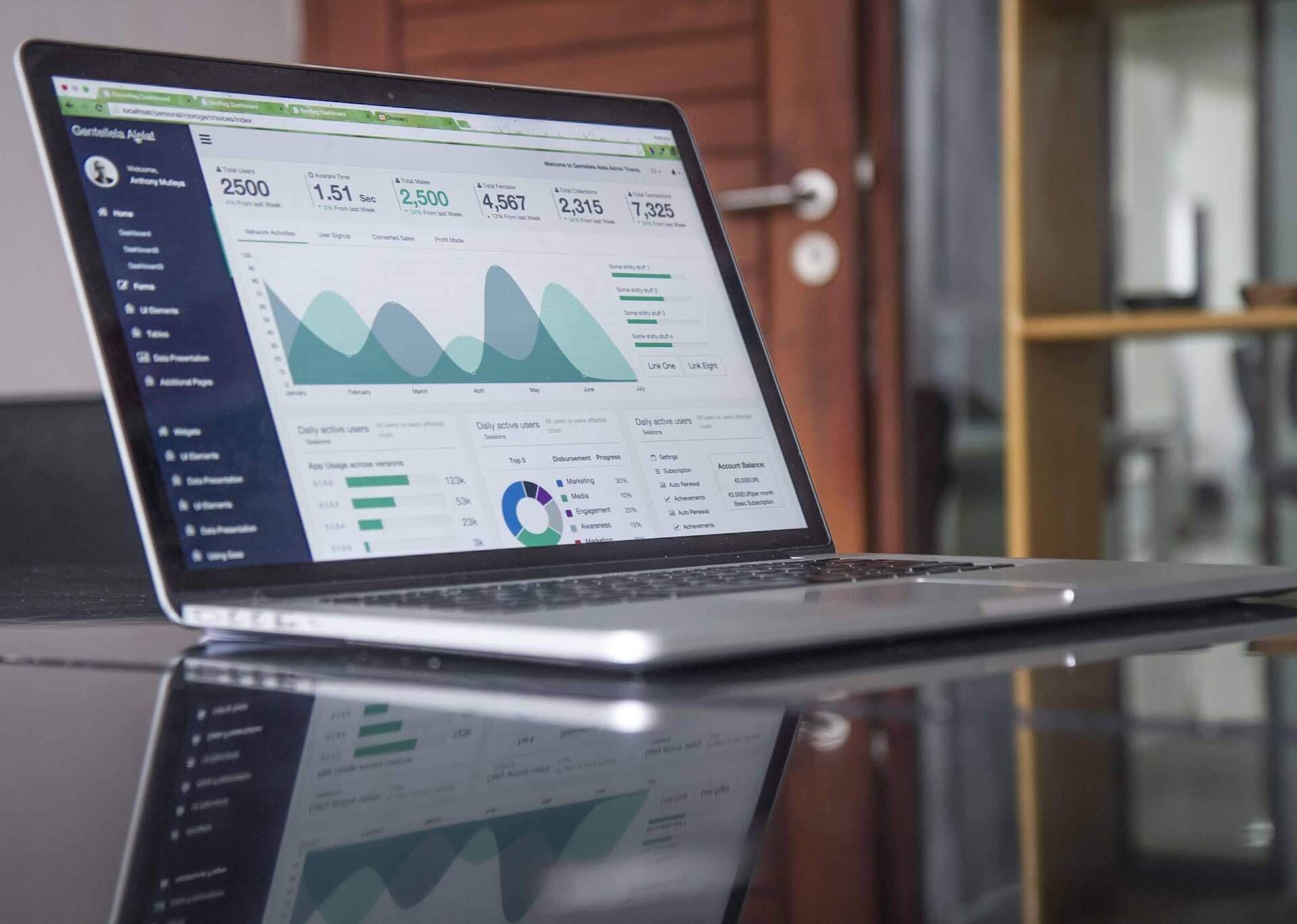 A laptop is open on the table. it is silver and has a screen open with various graphs and Analytics showing on the open page.