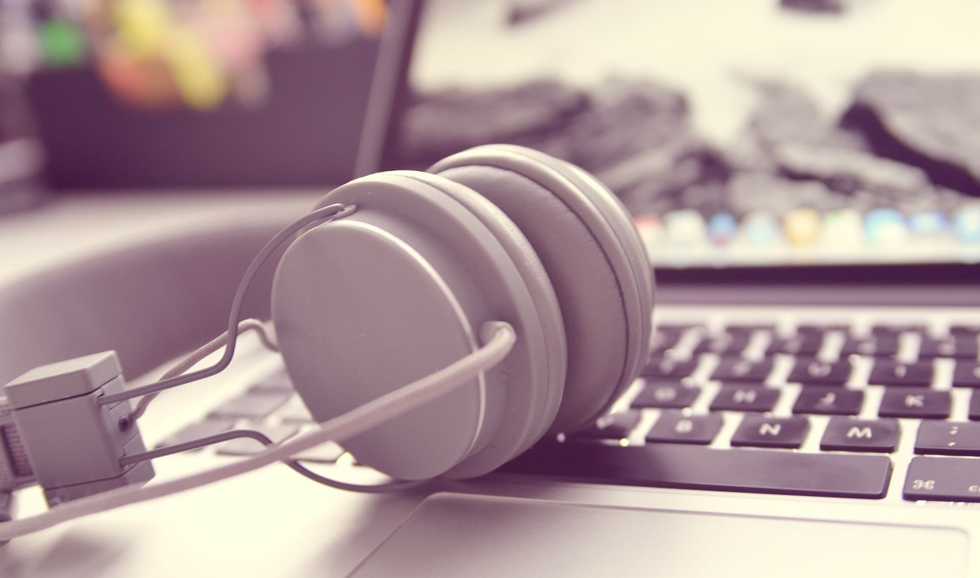 Image shows a close-up shot of a pain of grey headphones resting on an open laptop.