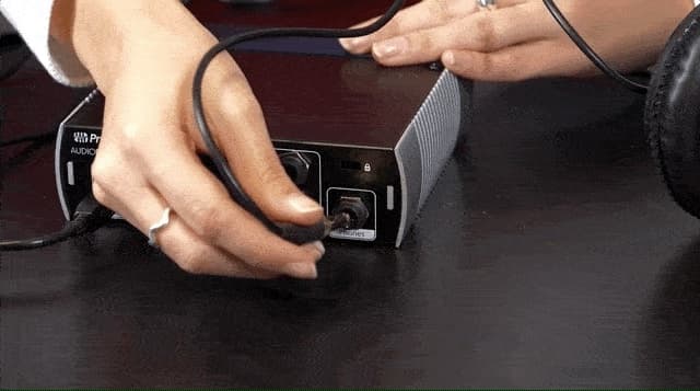 Image shows a pair of hands plugging in headphones into the 1/4" input on an audio interface.