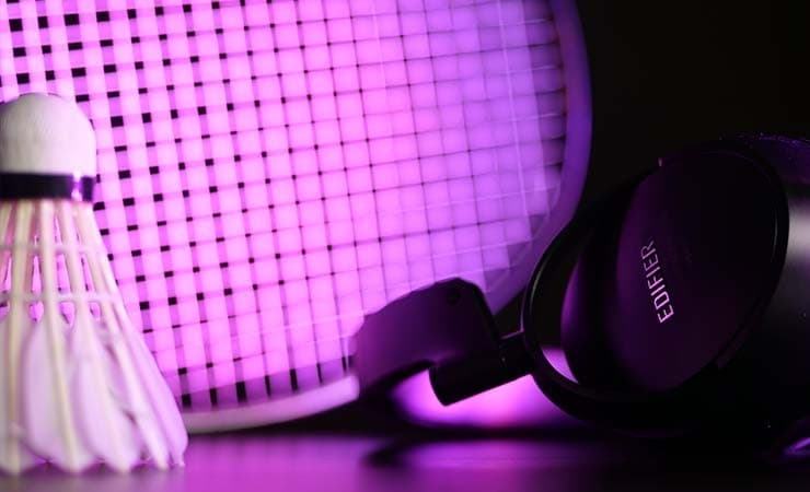 image shows a pair of headphones and badminton equipment lit up with purple light.