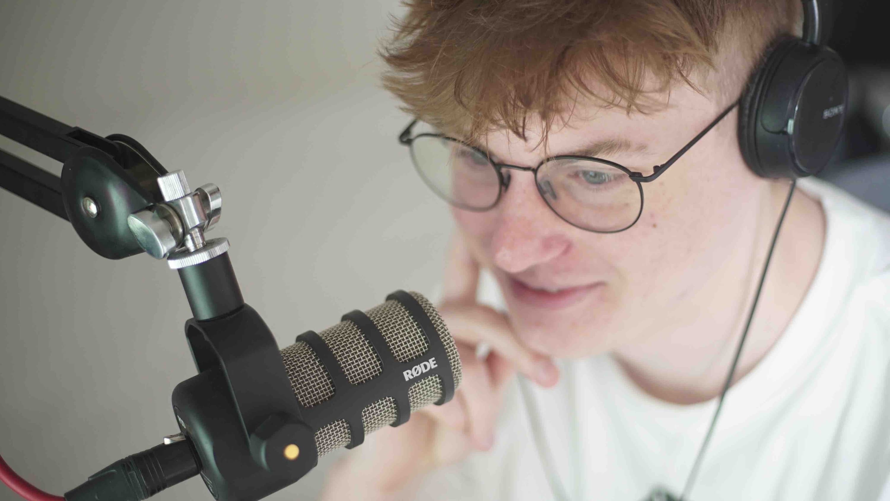 Image shows a young man wearing behind a microphone and wearing headphones.