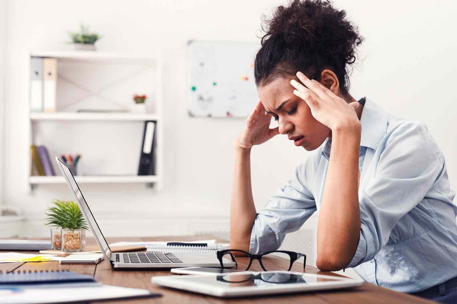 Image shows a woman in an office, with her head in her hands look exasperated.