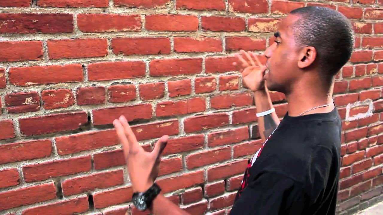 Image shows a man talking to himself next to a brick wall.