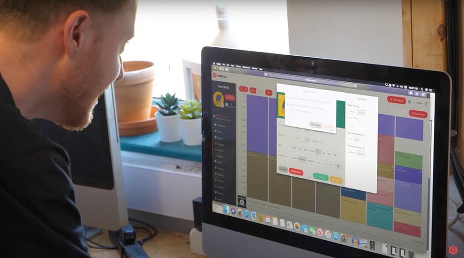 A white man looking down at a iMac, which is displaying the Radio.co