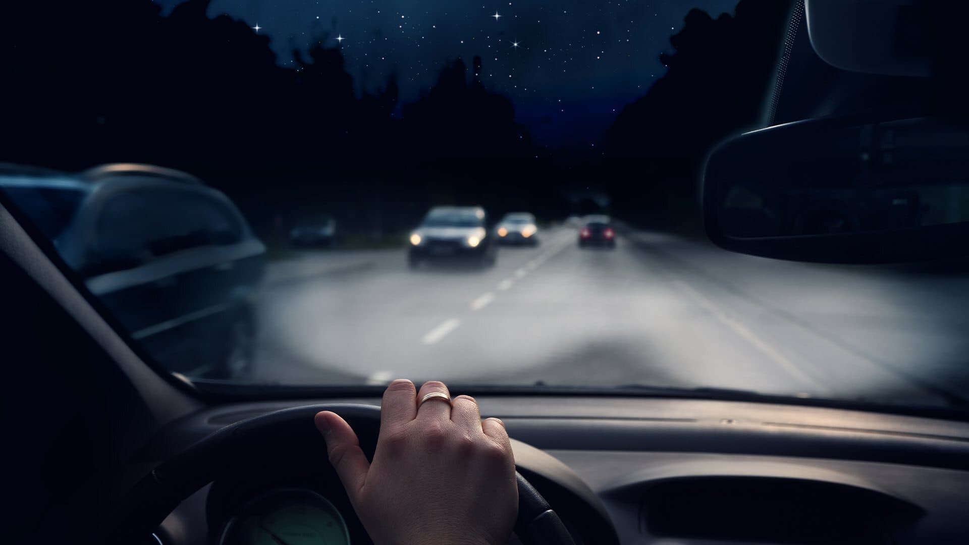 Image shows the view from a car dashboard as someone drives at night.