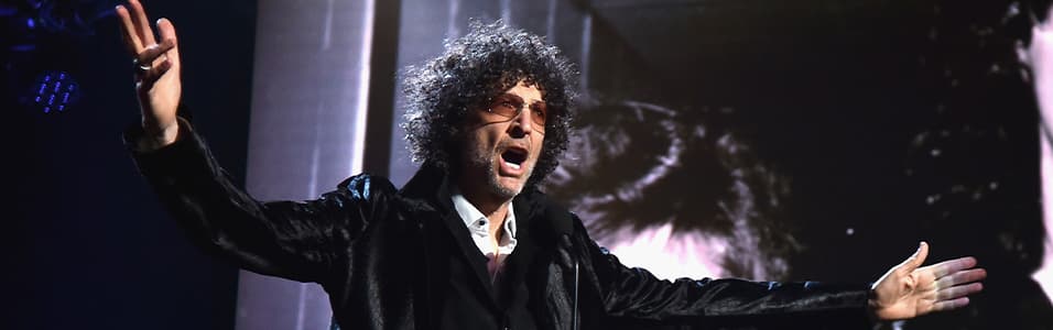 Image shows Howard Stern on stage, with his arms out wide.