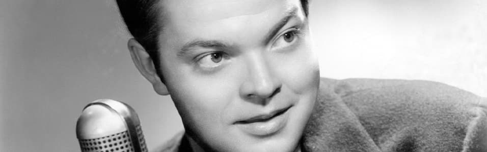 Image shows a black and white photo of a young Orson Welles next to a microphone.