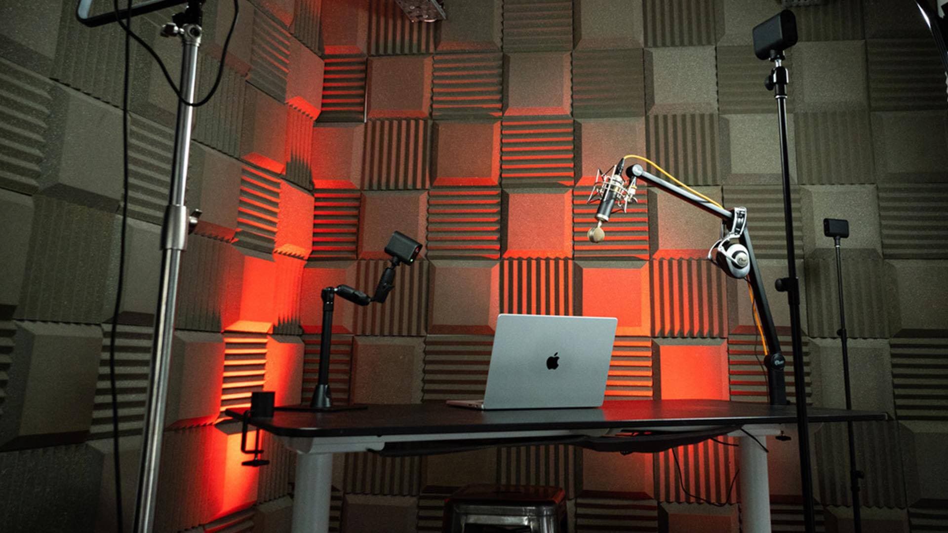 Image shows a filming space, with a laptop on a desk and lights, cameras and microphones angled around it.