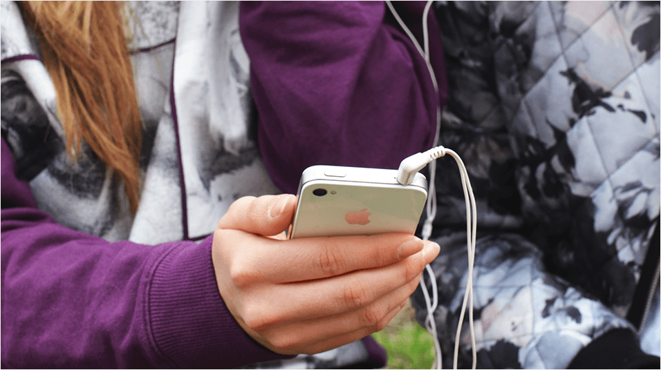 Image is a close-up of a woman listening to her iPhone using wired headphones.