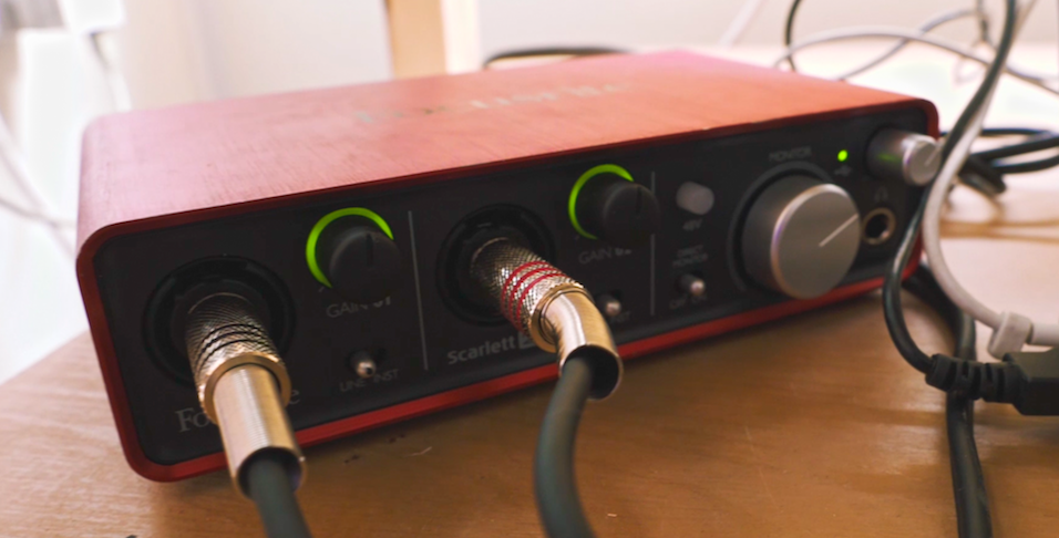 this is an image of a red and black audio interface, a small box with two cables input into it. Two dials are lit in green and a third dial is silver.