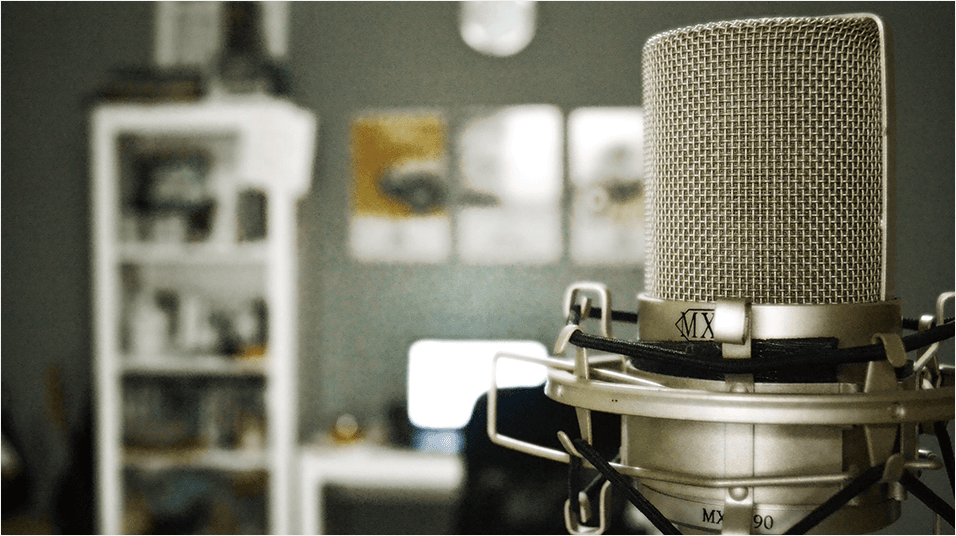 There is an olive green painted backdrop with a white bookcase visible on the left. On the right is a silver microphone zoomed in.