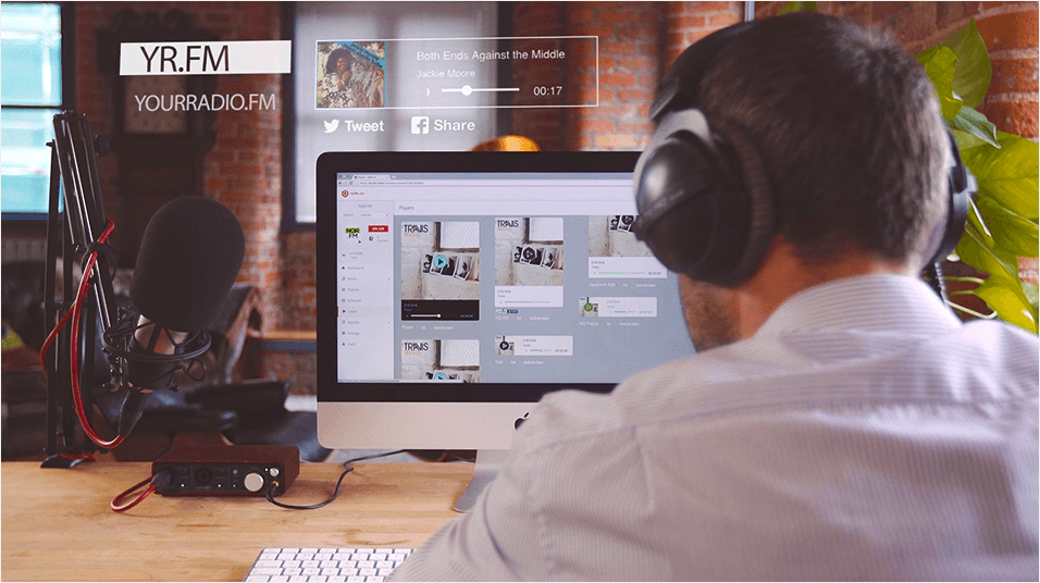 Image shows a man on a computer wearing headphones, on the screen is various visual branding assets.