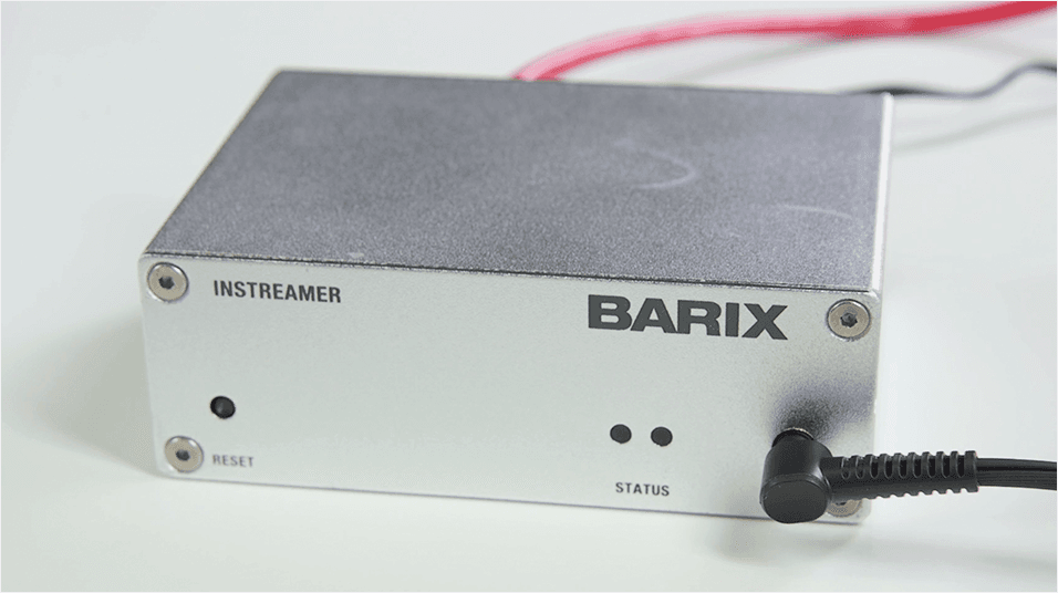 This is an image of the Barix Instreamer, a grey box with a cable plugged in and the word Barix emblazoned across it. It is on a white, neutral background.
