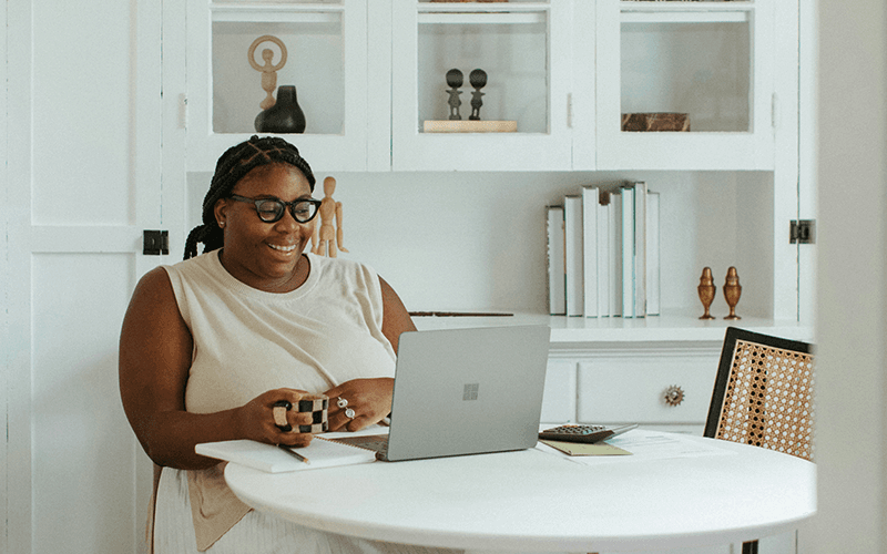 Image shows a woman working remotely and smiling at her computer.