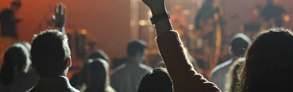 This is an image of an audience at a live event. It's silhouettes of arms in the air with an orange background.