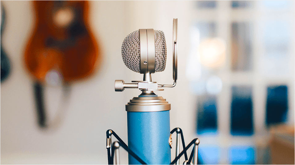 This is a neutral background with posters and a bedroom door in the back. The forefront of the image is a blue and silver microphone in the centre.