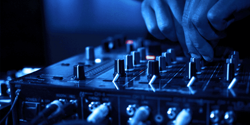 this is a dark blue image of fingers on a mixing desk. It appears to be in aclub or concert venue.