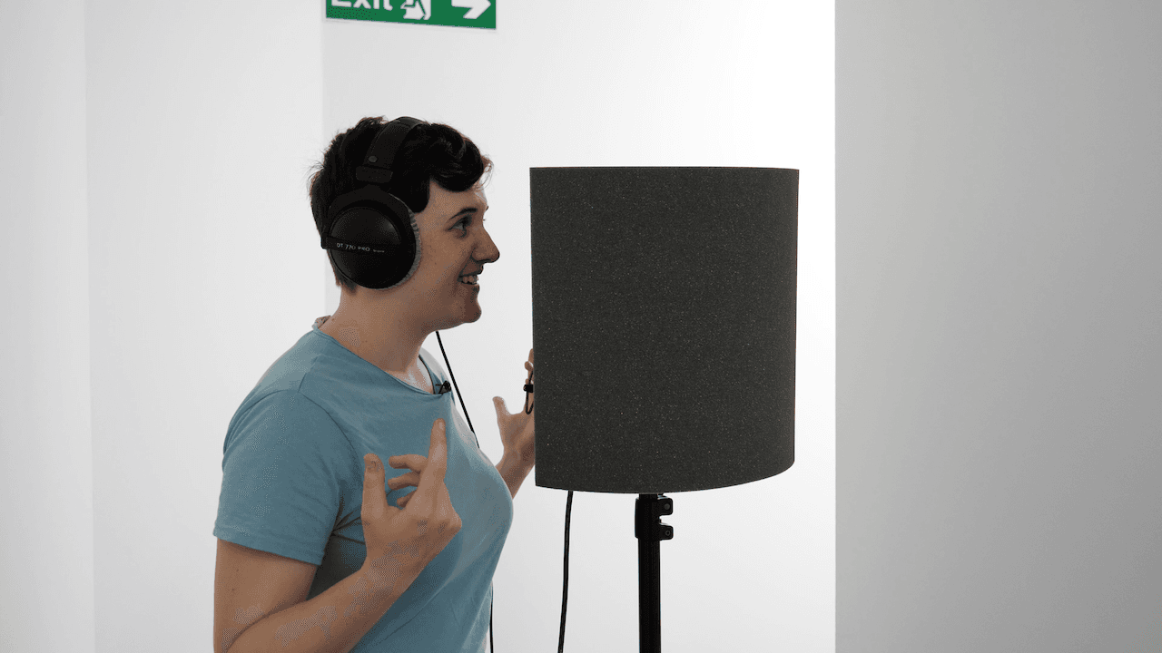 Image shows a woman speaking into a mic which has the Pro Acoustic Foam Microphone Screen around it.