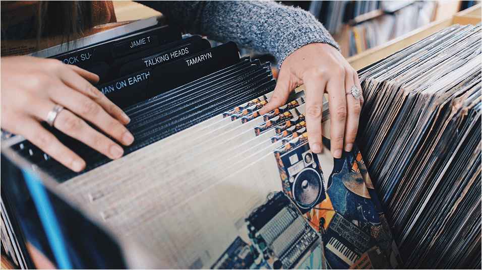 This is an image of white hands looking through vinyl records. They are resting on older ones and their fingers flick through white ones.