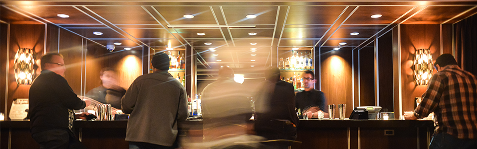 This is a blurred picture of a busy Hotel Bar. The picture is warmly lit and people are socialising within the image.