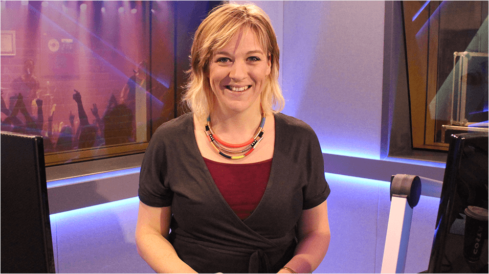 A blonde woman, Kate Cocker, smiles in the centre of the frame. She is in a studio.