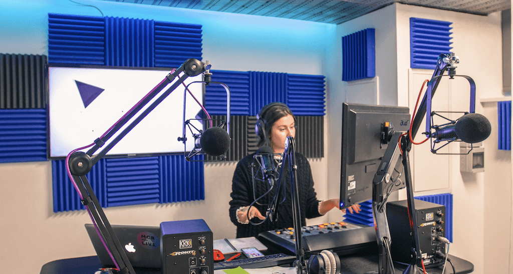 Image shows a woman presenting a radio show from a radio studio.