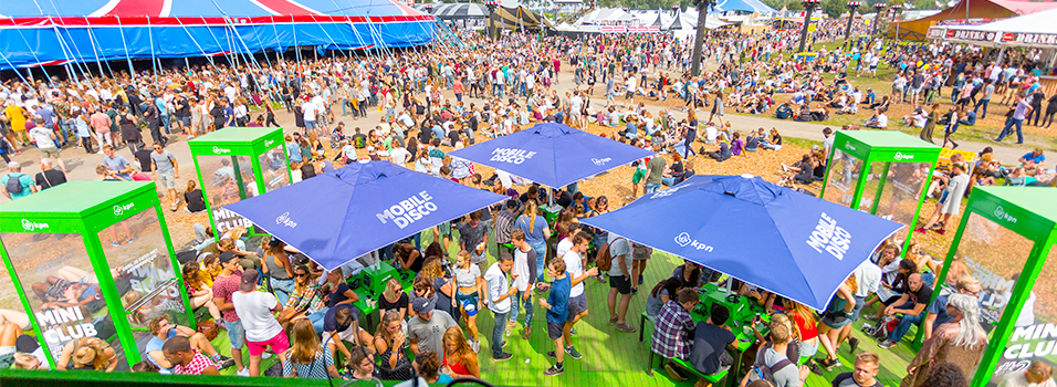 This is an image of the Silent Disco Radio Festival from an aerial view. There are lots of blue tents and stalls and thousands of people in the image with green booths visible.