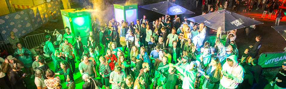 This is an aerial image of festivalgoers with green lighting on them. There are multiple people dancing at silver barriers.