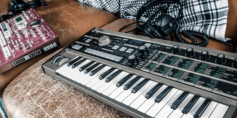 This is an image of a keyboard (black and white) on a leather brown sofa. On the left is a red mixing board with various knobs and features on it.