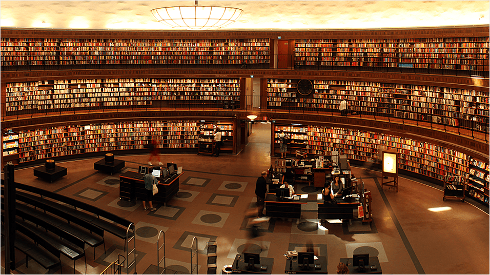 This is an image of a huge circular library, seemingly a massive university or college one, with plenty of books visible in warm light, and a mahogany colour scheme.