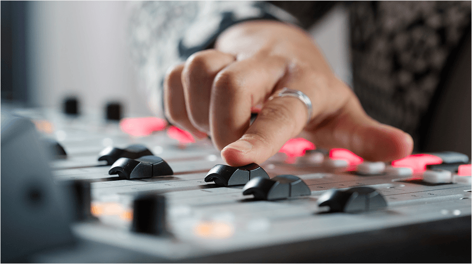 Image is a close-up shot of a hand pushing up a fader on a broadcasting desk.
