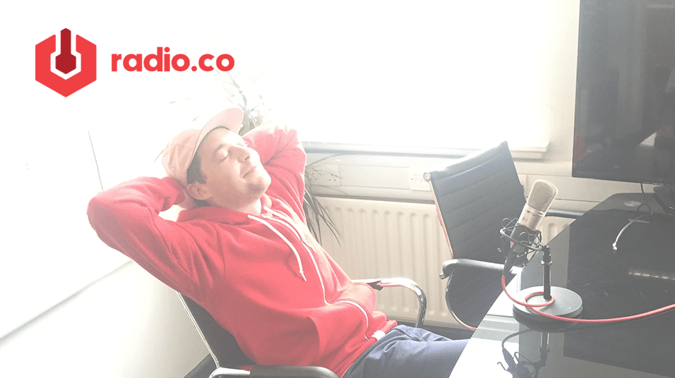 This is an image of a white man in a yellow cap leaning back on an office chair with his eyes shut. He is wearing a red hoodie. Above him is a radio.co logo and the white background is also faded slightly.