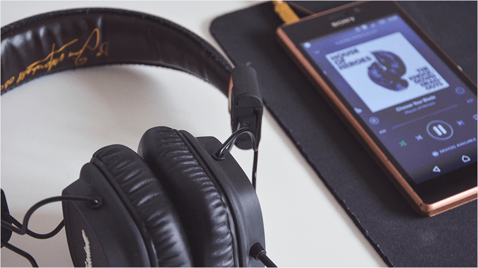 Image shows an Android phone playing music with a pair of headphones next to it, on a desk.