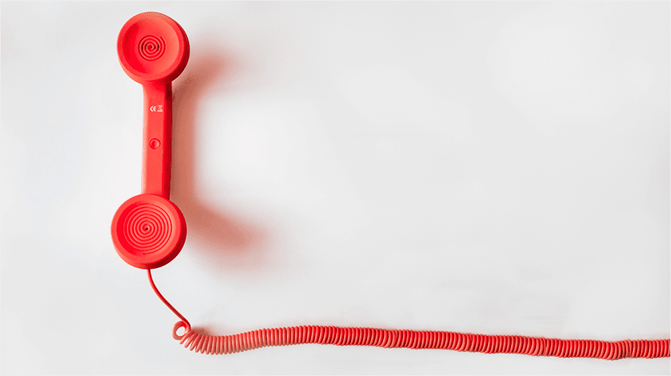 This is an image of a red telephone and corresponding spiralled wire. The phone has a shadow. This image has a neutral white backdrop.